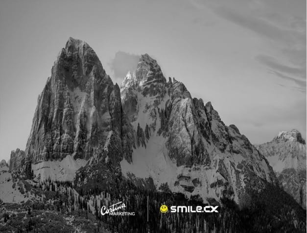 Siyah-beyaz karlı Dolomit zirveleri; alt kısımda Cortina Marketing ve smile.cx logoları yan yana.